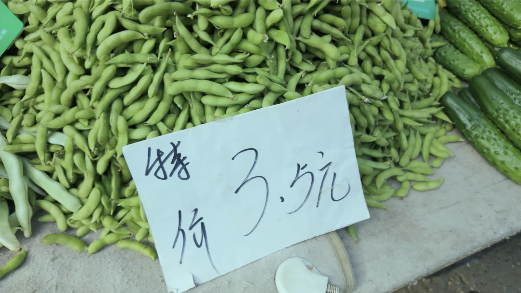 Pile of fresh edamame pods at a market with a handwritten paper price sign