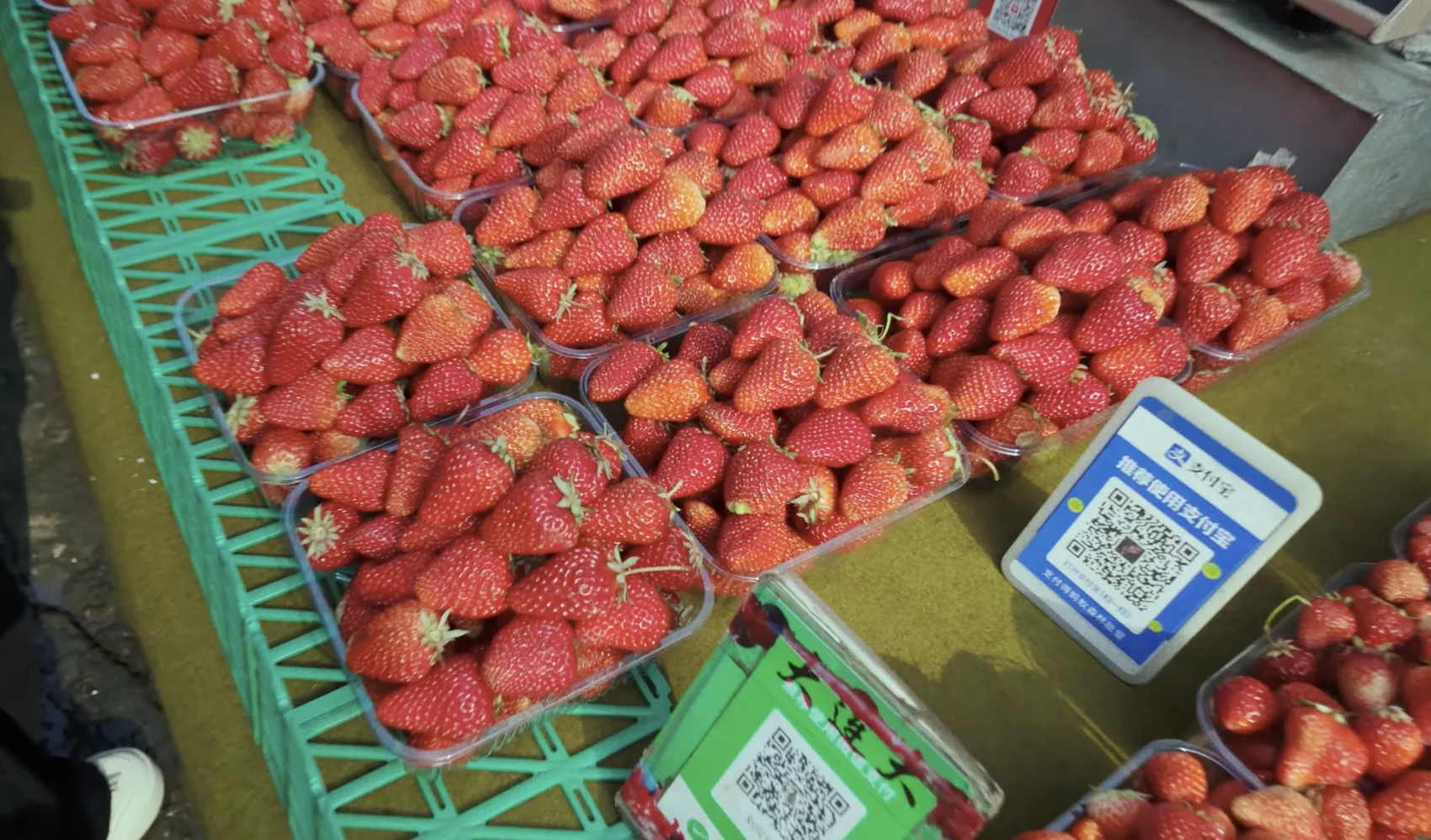Punnets of strawberries at a market with a blue Alipay QR payment card propped between them