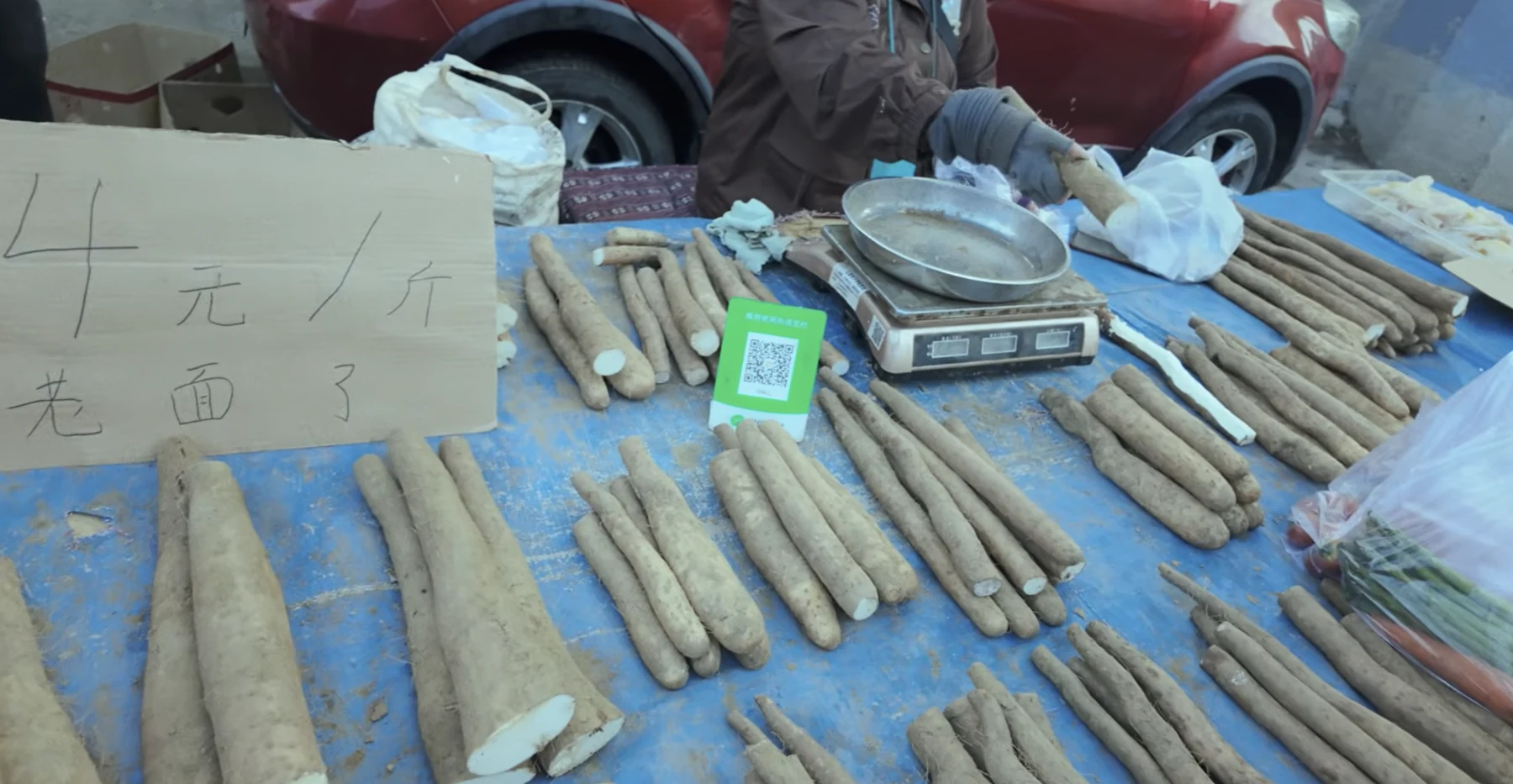 Long Chinese yam roots laid on a table with a cardboard sign reading 4 yuan per jin